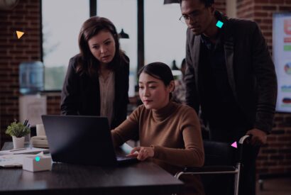 Team of 3 people collaborating around a laptop in an office, planning website maintenance services for WordPress clients.